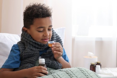 African-American boy taking cough syrup on bed at home, space for text. Cold medicine