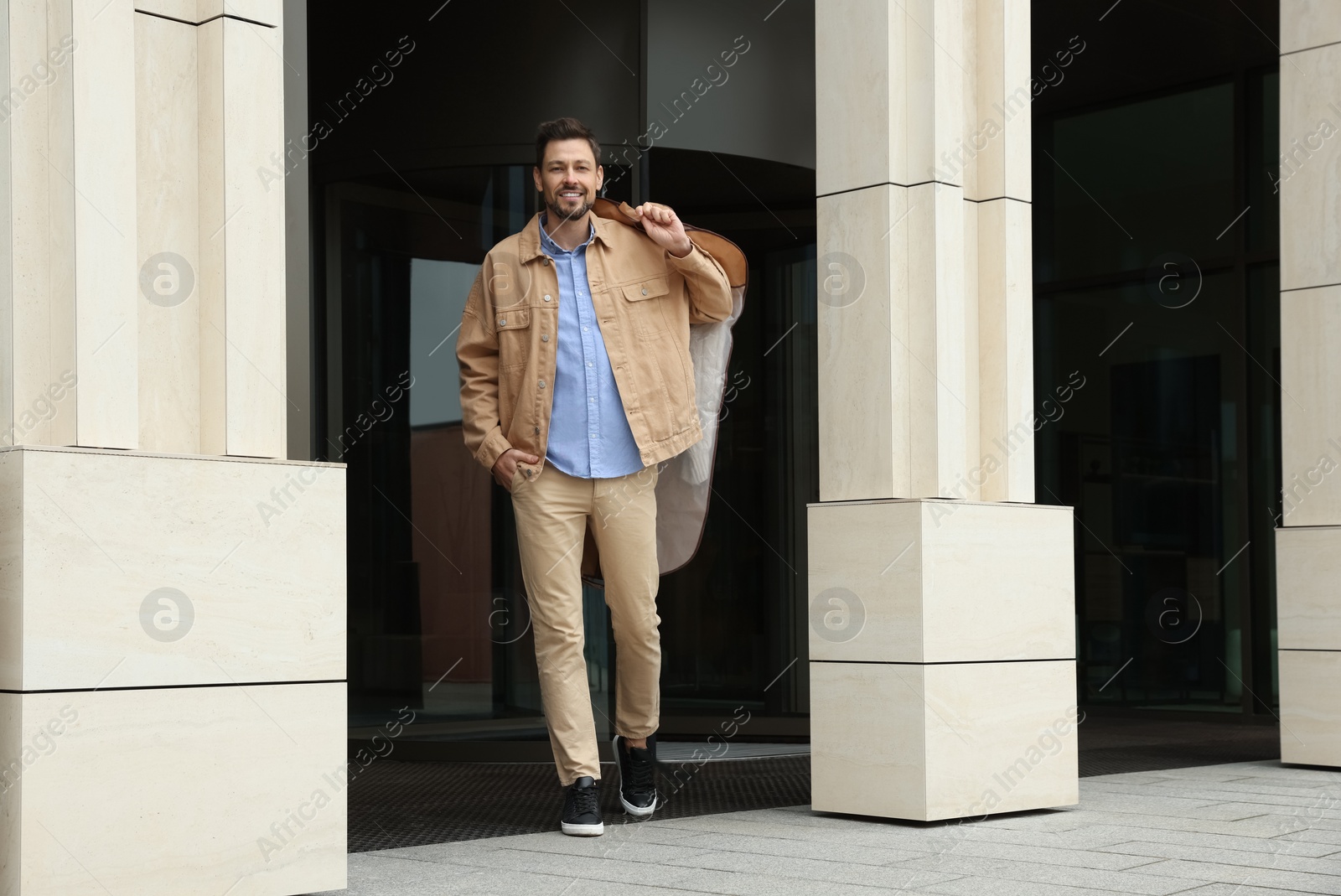 Photo of Attractive happy man holding garment cover with clothes outdoors. Dry cleaning service