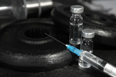 Vials and syringe with drug near sports equipment on table, closeup. Doping control