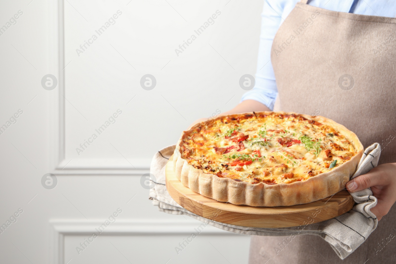 Photo of Woman holding board with tasty quiche indoors, closeup. Space for text