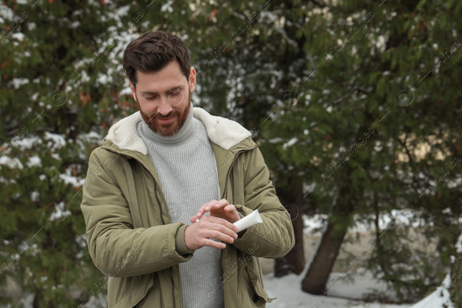 Photo of Man applying cream from tube onto hand outdoors, space for text. Winter care