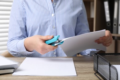 Photo of Woman stapling papers at wooden table indoors, closeup