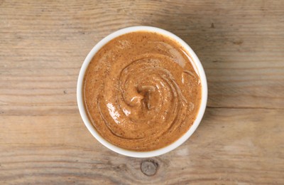 Delicious nut butter in bowl on wooden table, top view