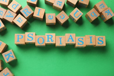 Photo of Word Psoriasis made of wooden cubes with letters on green background, flat lay