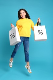Image of Discount, sale, offer. Woman jumping with shopping bags against light blue background. Paper bags with percent signs