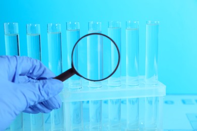 Photo of Scientist with magnifying glass examining test tubes in laboratory, closeup. Color tone effect