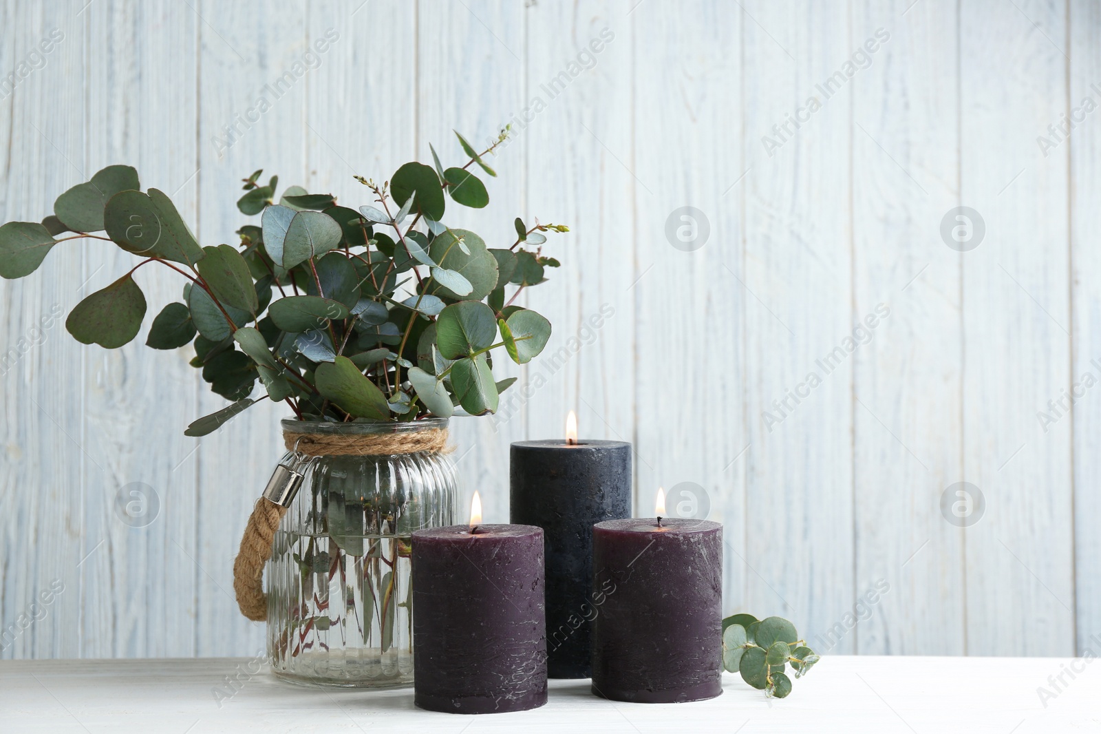 Photo of Burning candles and green branches on white table