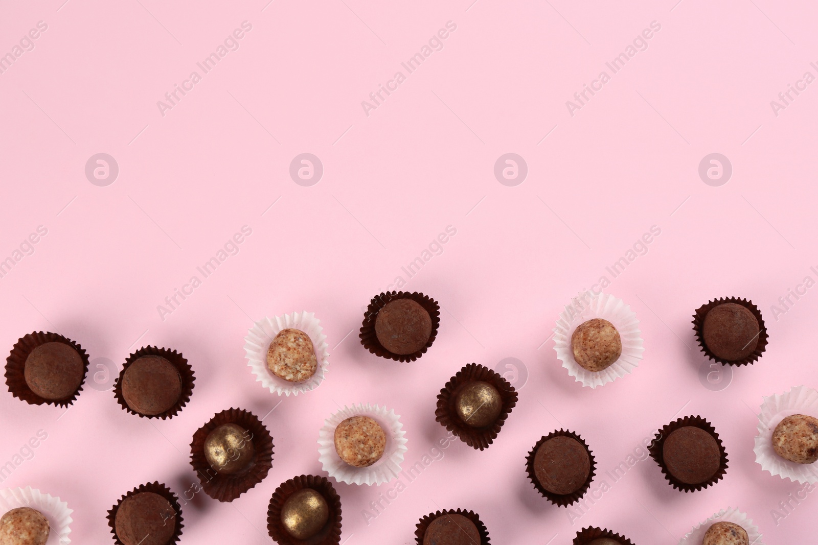 Photo of Different delicious chocolate candies on light pink background, flat lay. Space for text