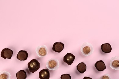 Different delicious chocolate candies on light pink background, flat lay. Space for text