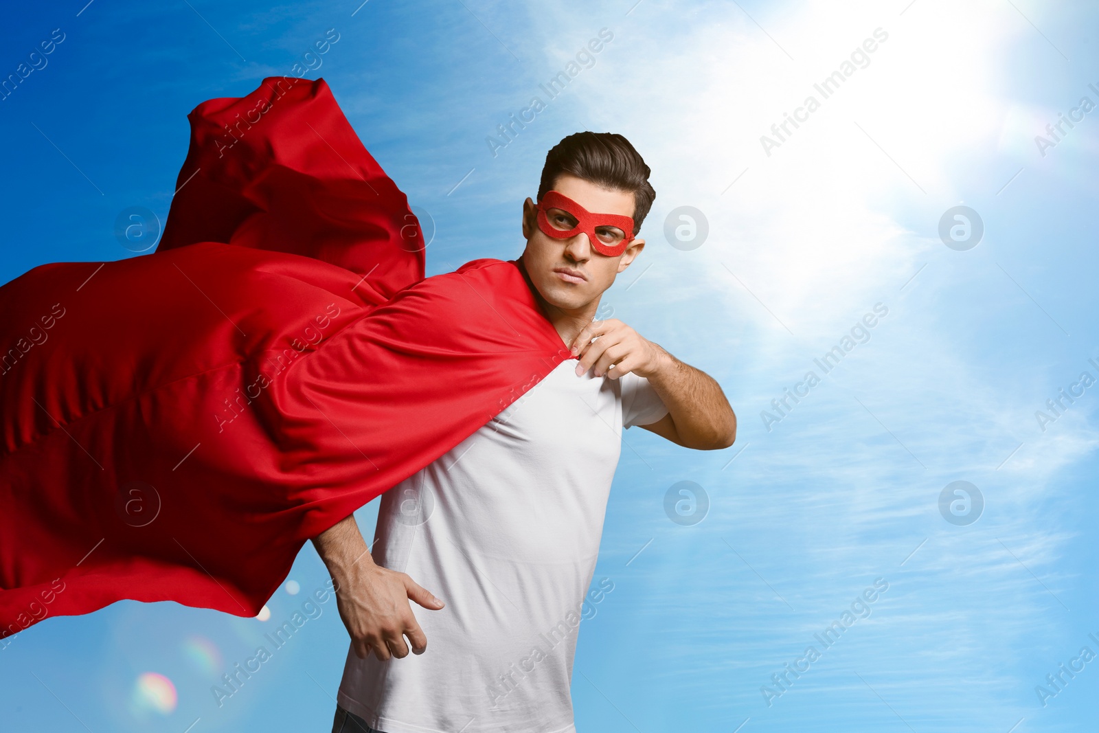 Image of Man wearing superhero cape and mask against blue sky, space for text