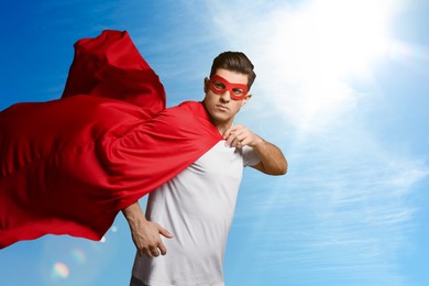 Image of Man wearing superhero cape and mask against blue sky, space for text
