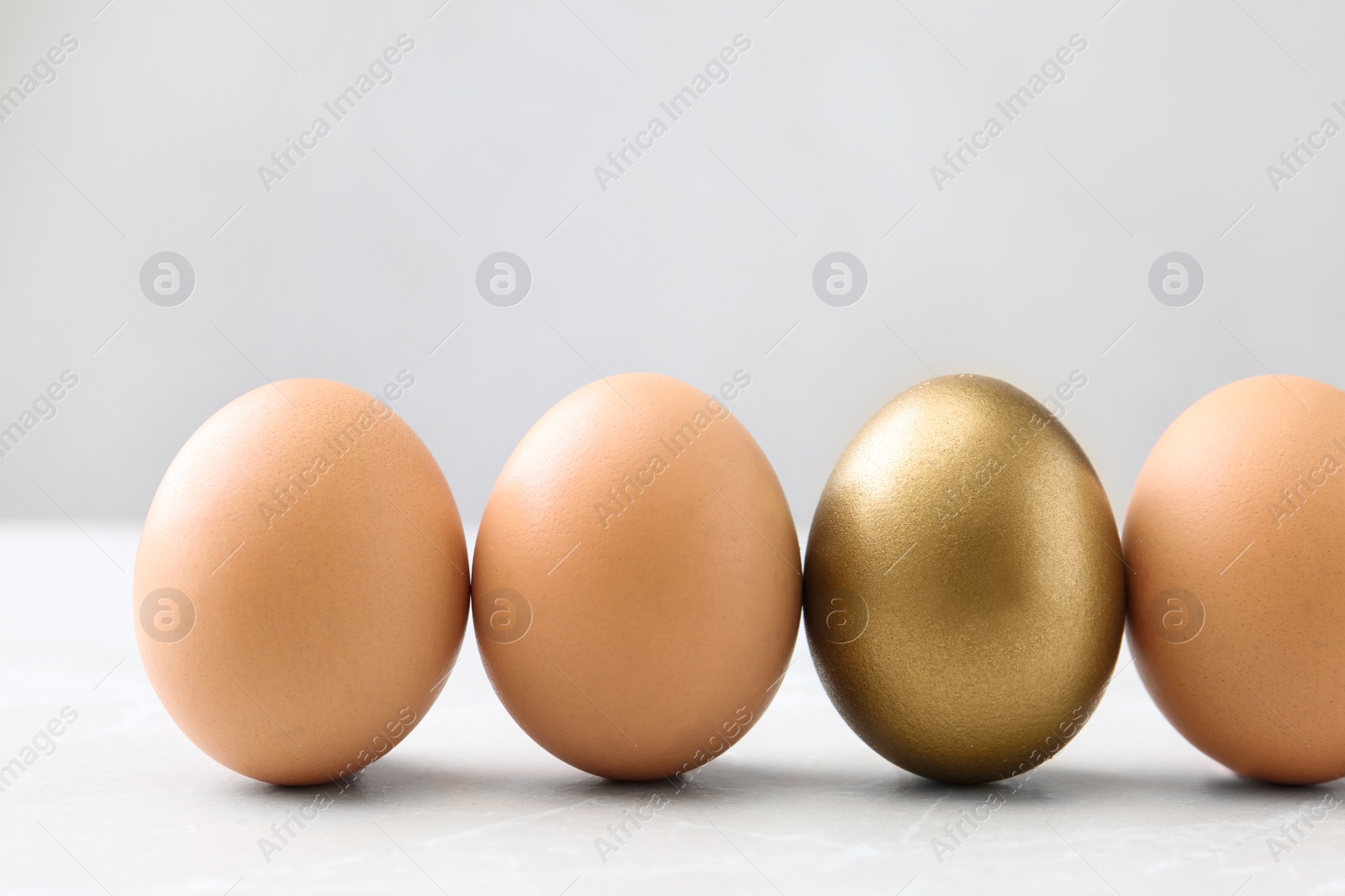 Photo of Golden egg among others on white table