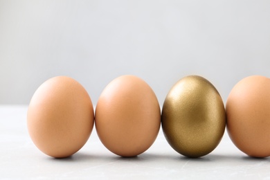 Golden egg among others on white table