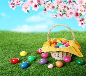 Image of Wicker basket with Easter eggs on green grass outdoors, space for text