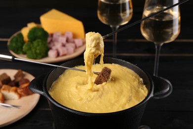 Photo of Dipping pieces of ham and bread into fondue pot with melted cheese on table, closeup