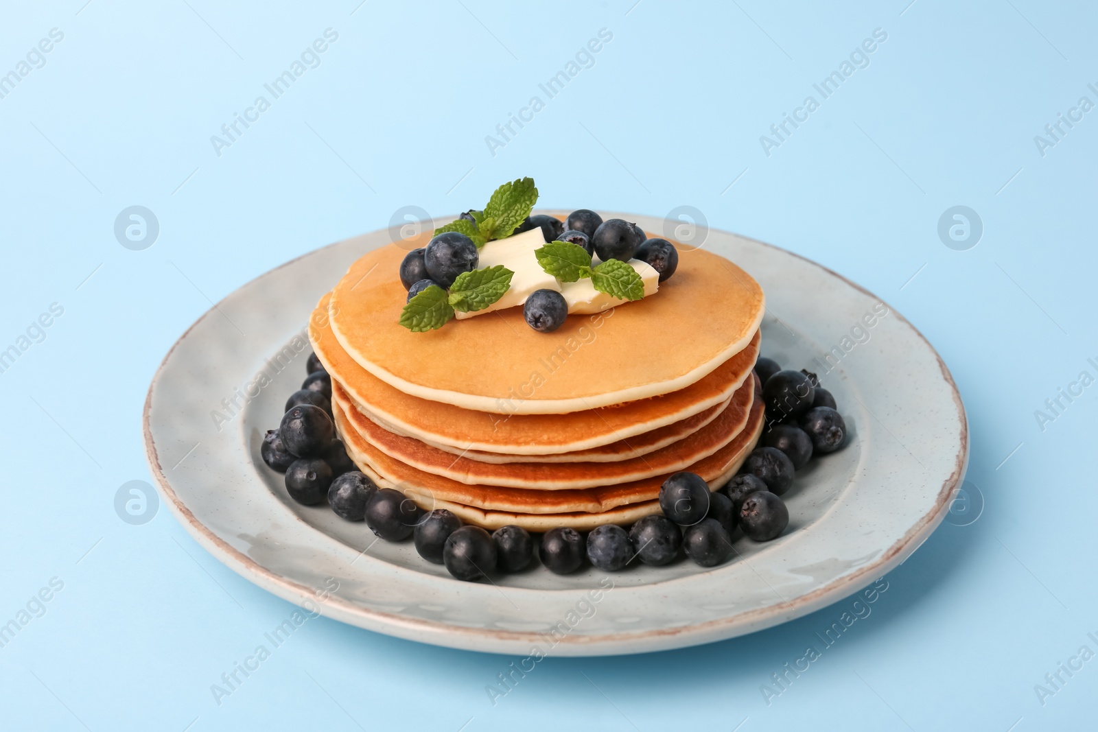 Photo of Stack of tasty pancakes with blueberries, butter and mint on light blue background