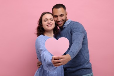 Photo of Lovely couple with paper heart on pink background. Valentine's day celebration