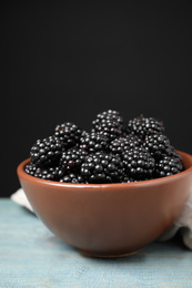 Photo of Fresh ripe blackberries in bowl on blue wooden table against dark background, closeup. Space for text