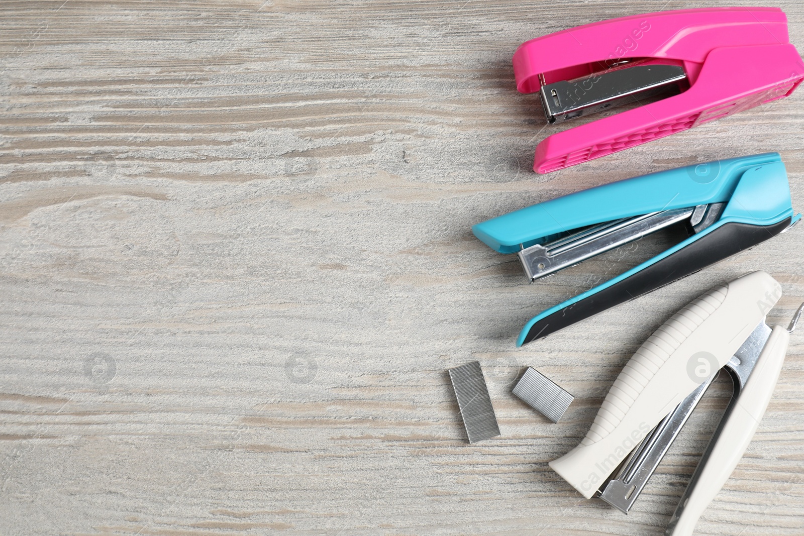 Photo of Color staplers and metal staples on wooden table, flat lay. Space for text