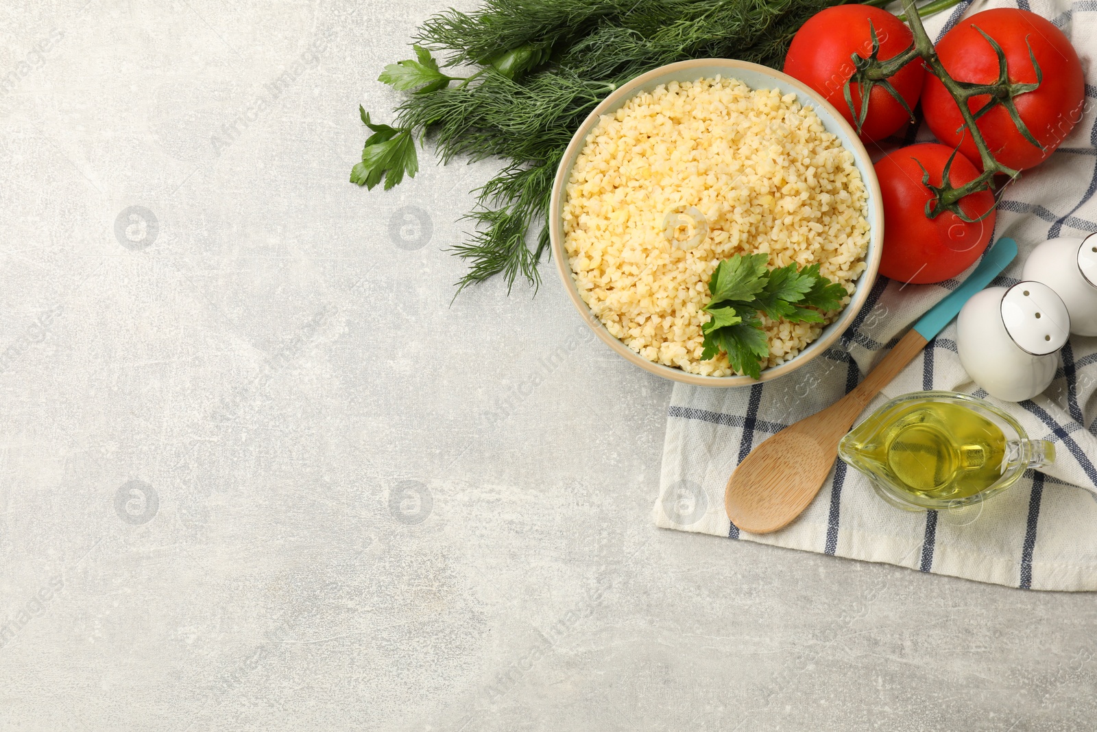 Photo of Delicious bulgur with parsley, dill, oil and tomatoes on light grey table, top view. Space for text