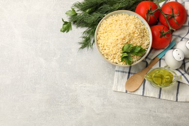 Photo of Delicious bulgur with parsley, dill, oil and tomatoes on light grey table, top view. Space for text