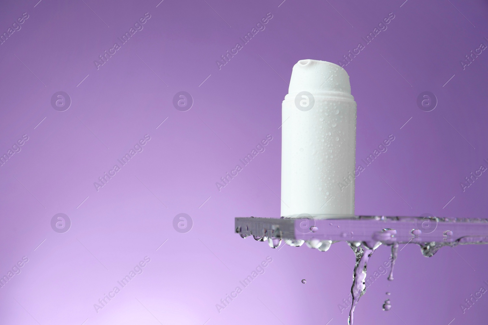 Photo of Moisturizing cream in bottle on glass with water drops against violet background. Space for text