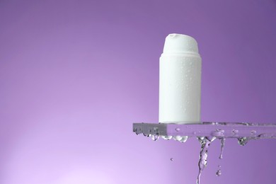 Moisturizing cream in bottle on glass with water drops against violet background. Space for text