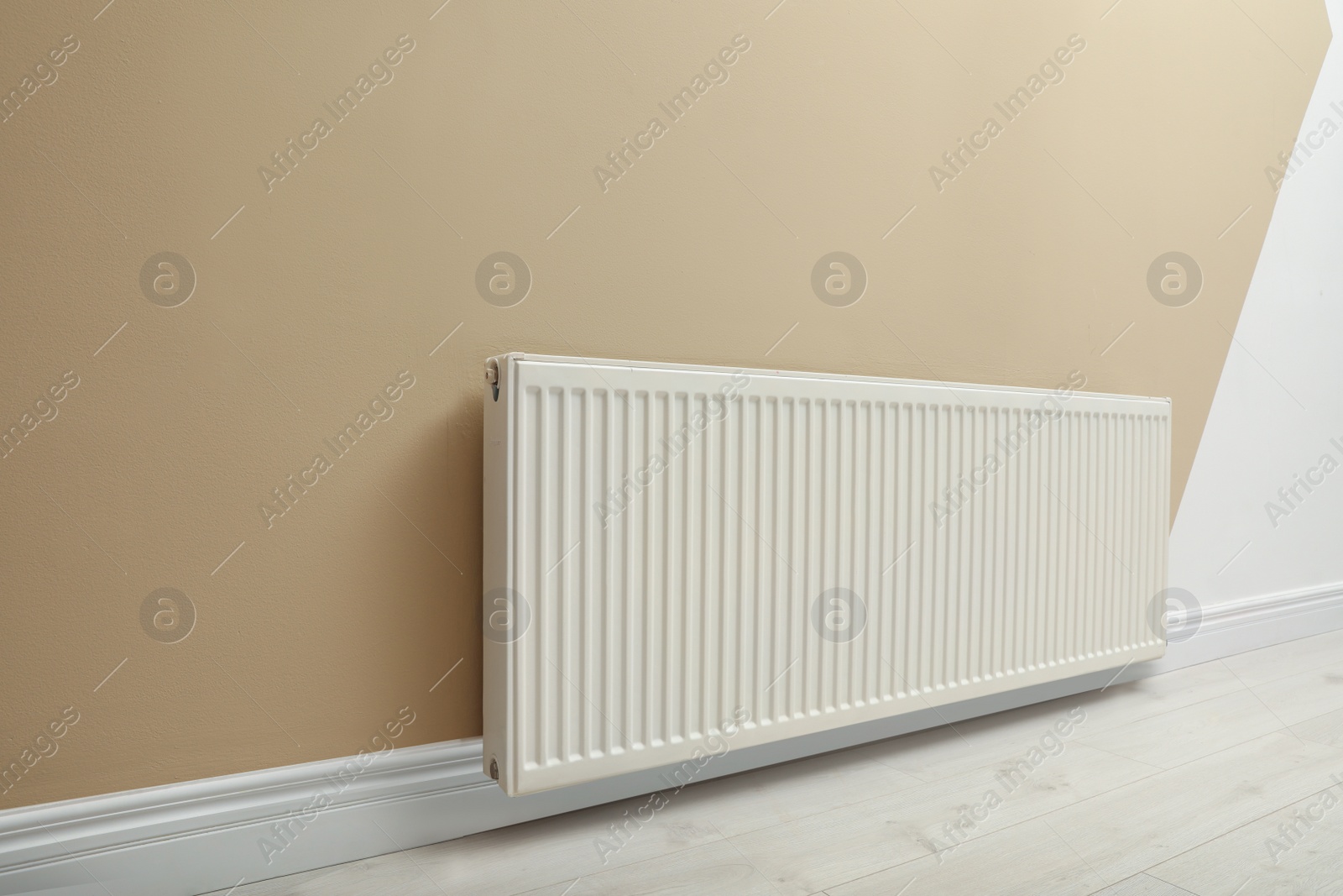 Photo of Modern radiator on beige wall indoors. Central heating system