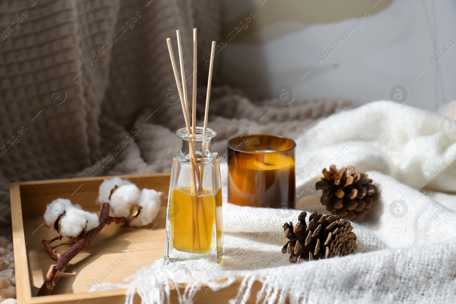 Photo of Reed air freshener, candle and pine cones on wooden tray indoors