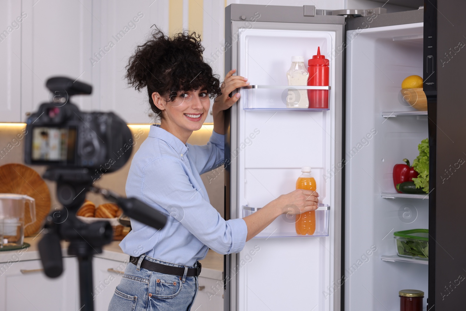 Photo of Smiling food blogger with bottle of juice recording video in kitchen