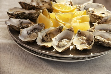 Fresh oysters with cut juicy lemon on plate, closeup