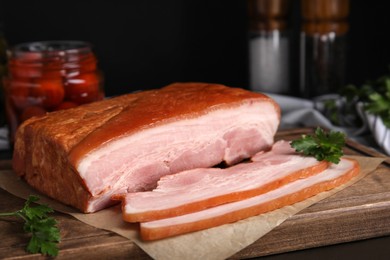 Photo of Delicious smoked bacon with parsley on wooden board, closeup