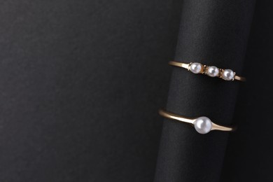 Photo of Elegant pearl rings on black background, top view. Space for text