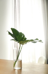 Photo of Green tropical leaves in vase on table. Modern decor for stylish interior