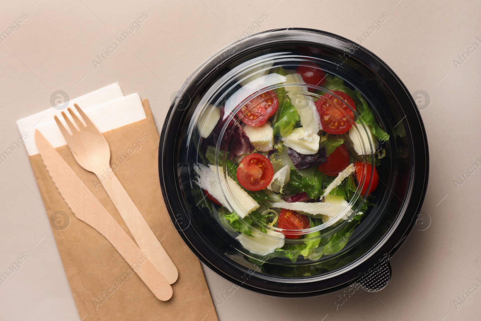 Photo of Tasty food in container with wooden fork and knife on light background, flat lay