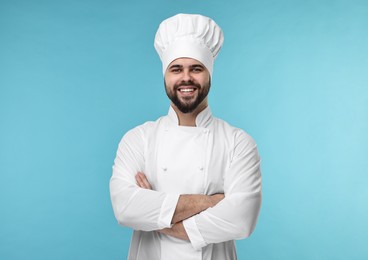 Happy young chef in uniform on light blue background