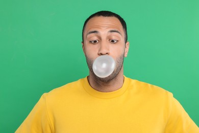 Photo of Portrait of young man blowing bubble gum on green background
