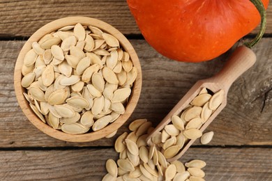 Bowl, scoop with seeds and fresh pumpkin on wooden table, flat lay