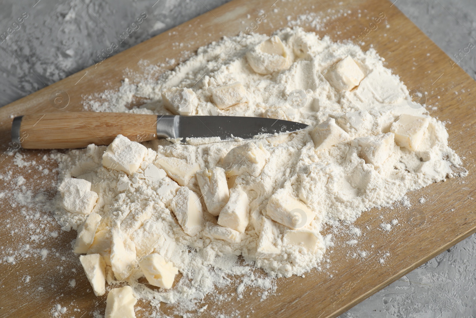 Photo of Making shortcrust pastry. Flour, butter, knife and wooden board on grey table