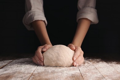 Woman kneading dough at table on dark background, closeup