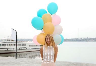 Photo of Beautiful young woman with bunch of balloons outdoors