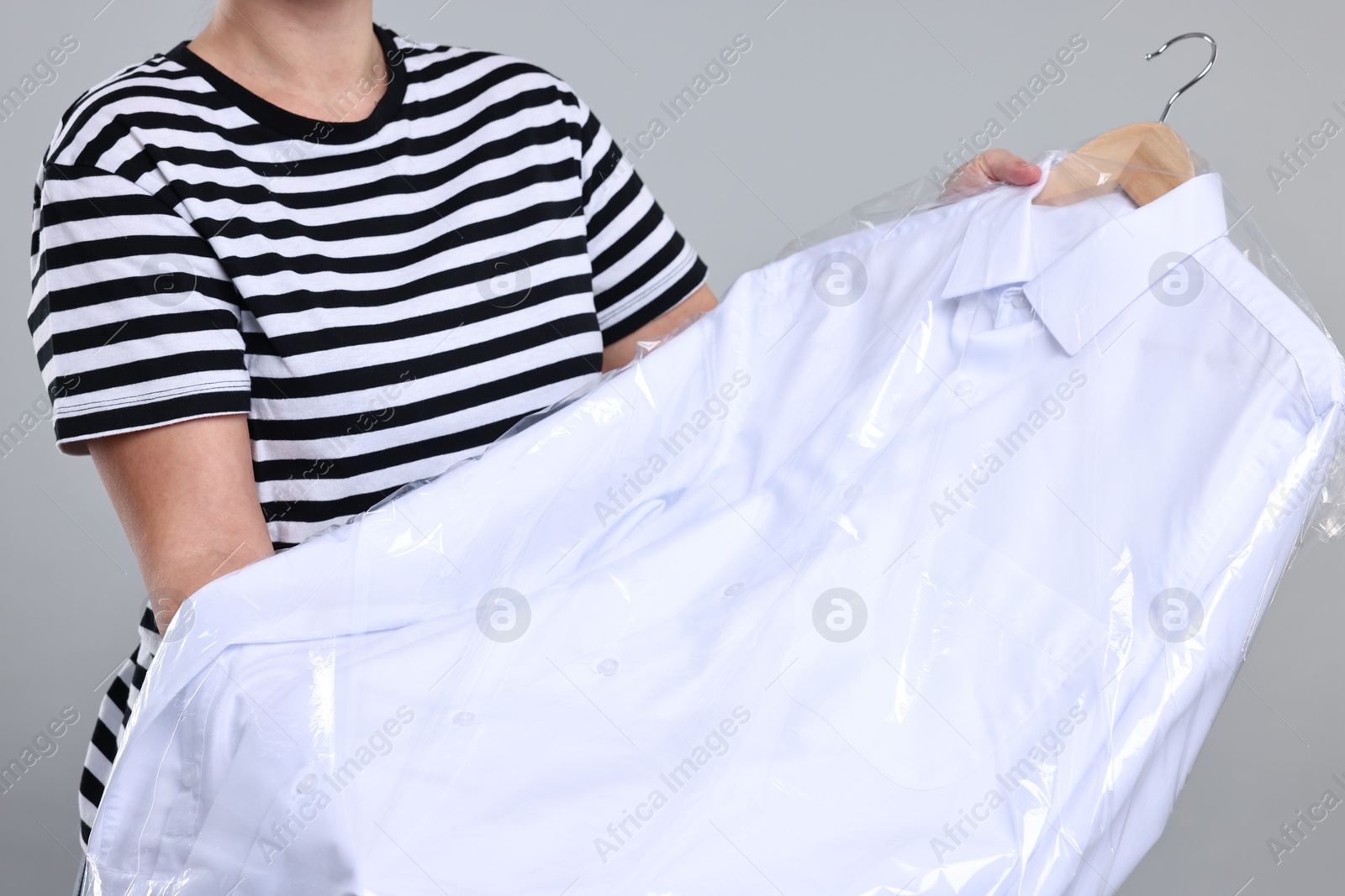 Photo of Dry-cleaning service. Woman holding shirt in plastic bag on gray background, closeup