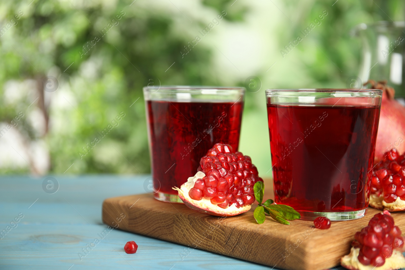 Photo of Pomegranate juice and fresh fruits on light blue wooden table outdoors, space for text