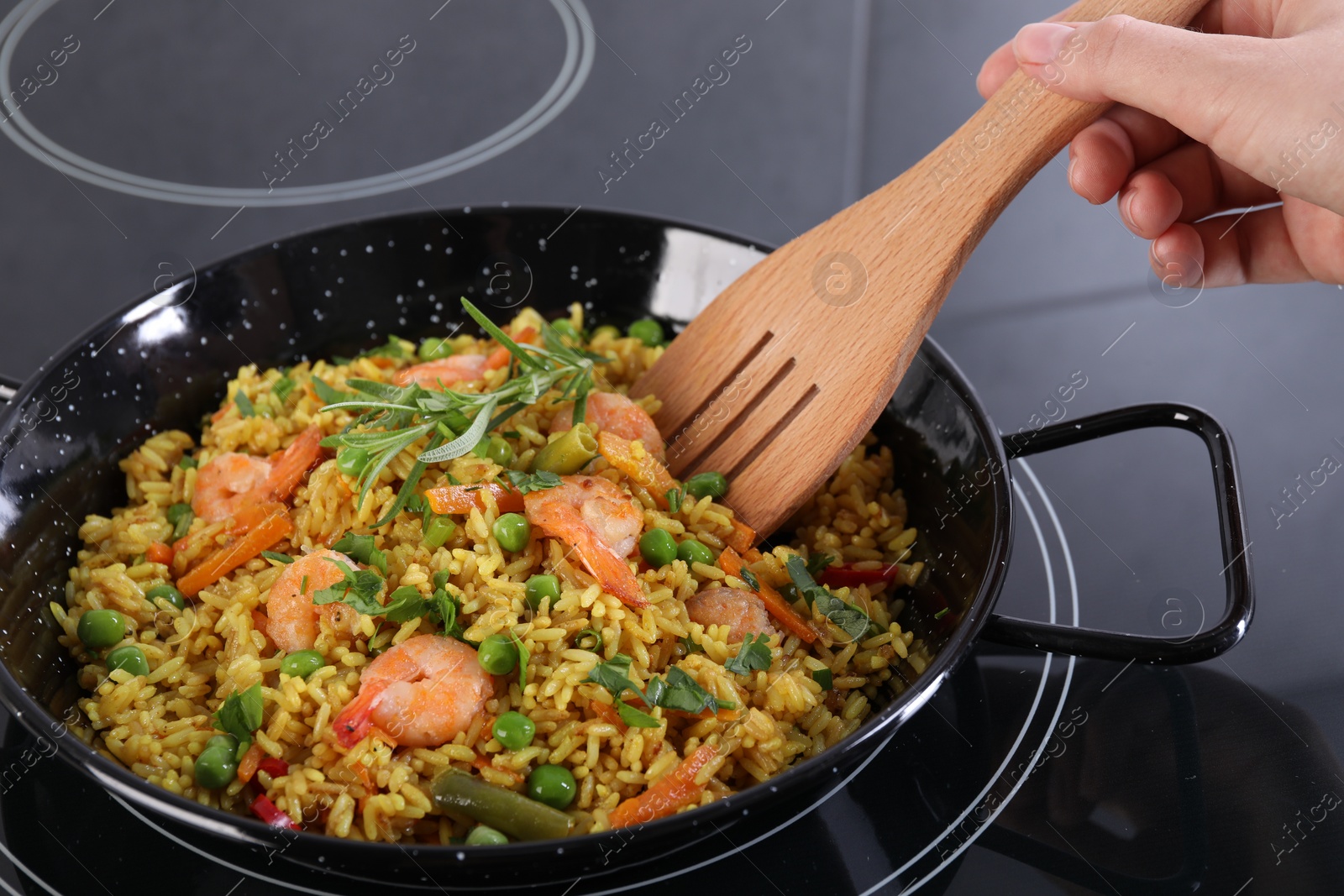 Photo of Woman cooking tasty rice with shrimps and vegetables on induction stove, closeup