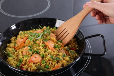 Photo of Woman cooking tasty rice with shrimps and vegetables on induction stove, closeup