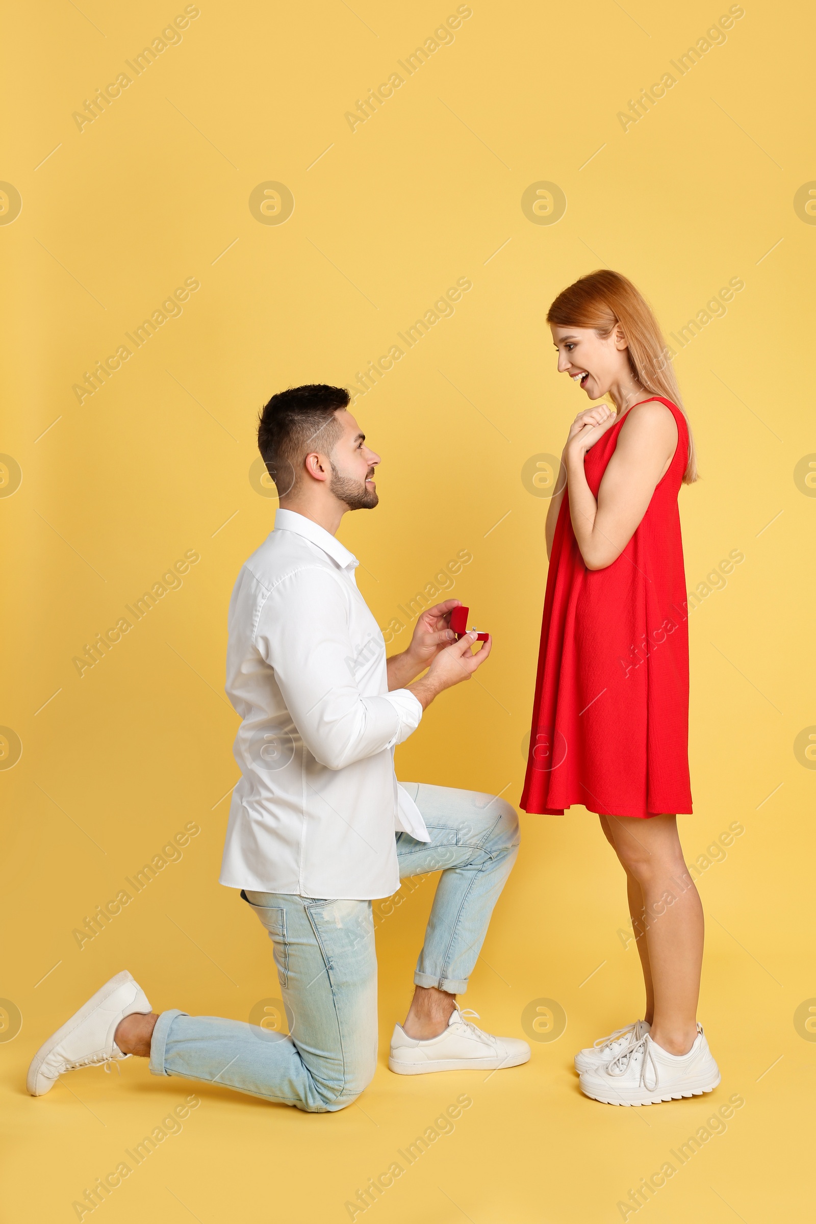 Photo of Man with engagement ring making marriage proposal to girlfriend on yellow background