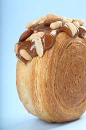 Photo of One supreme croissant with chocolate paste and nuts on light blue background, closeup. Tasty puff pastry