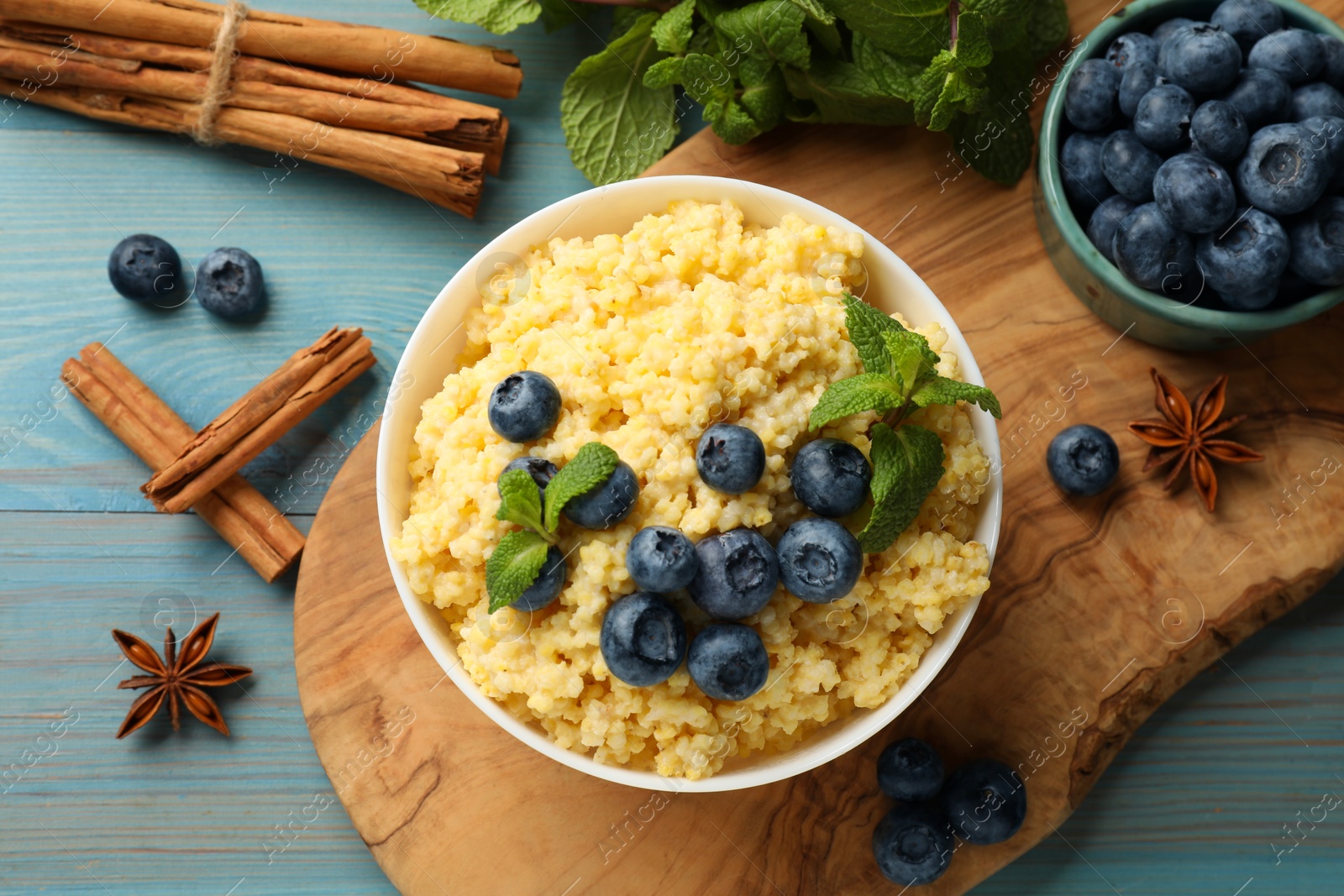 Photo of Tasty millet porridge with blueberries and mint in bowl on light blue wooden table, flat lay