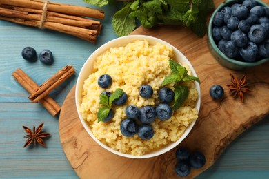 Photo of Tasty millet porridge with blueberries and mint in bowl on light blue wooden table, flat lay