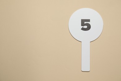 Photo of Auction paddle with number 5 on beige background, top view. Space for text